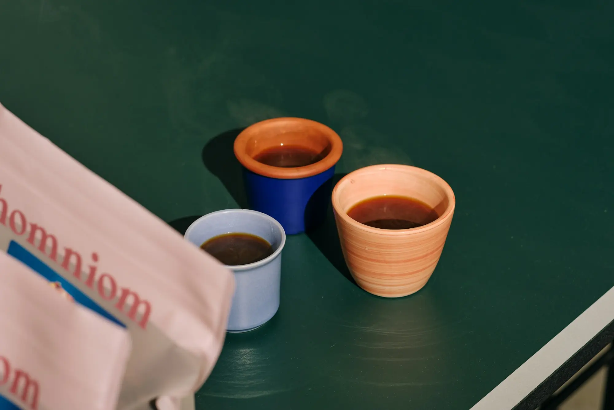 Three small cups of coffee beside a pink coffee bag on a green table