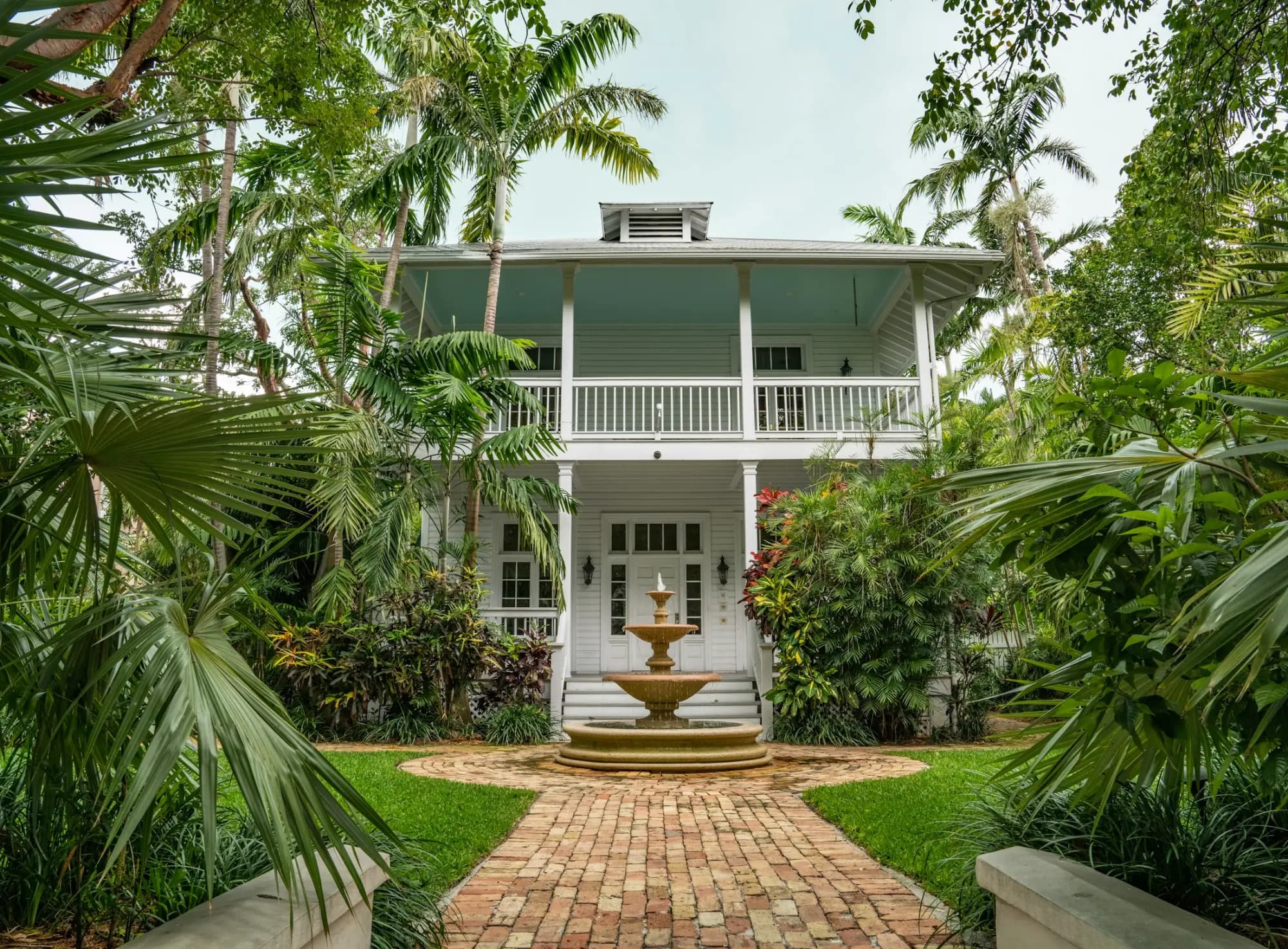 The white veranda house behind a fountain and palms