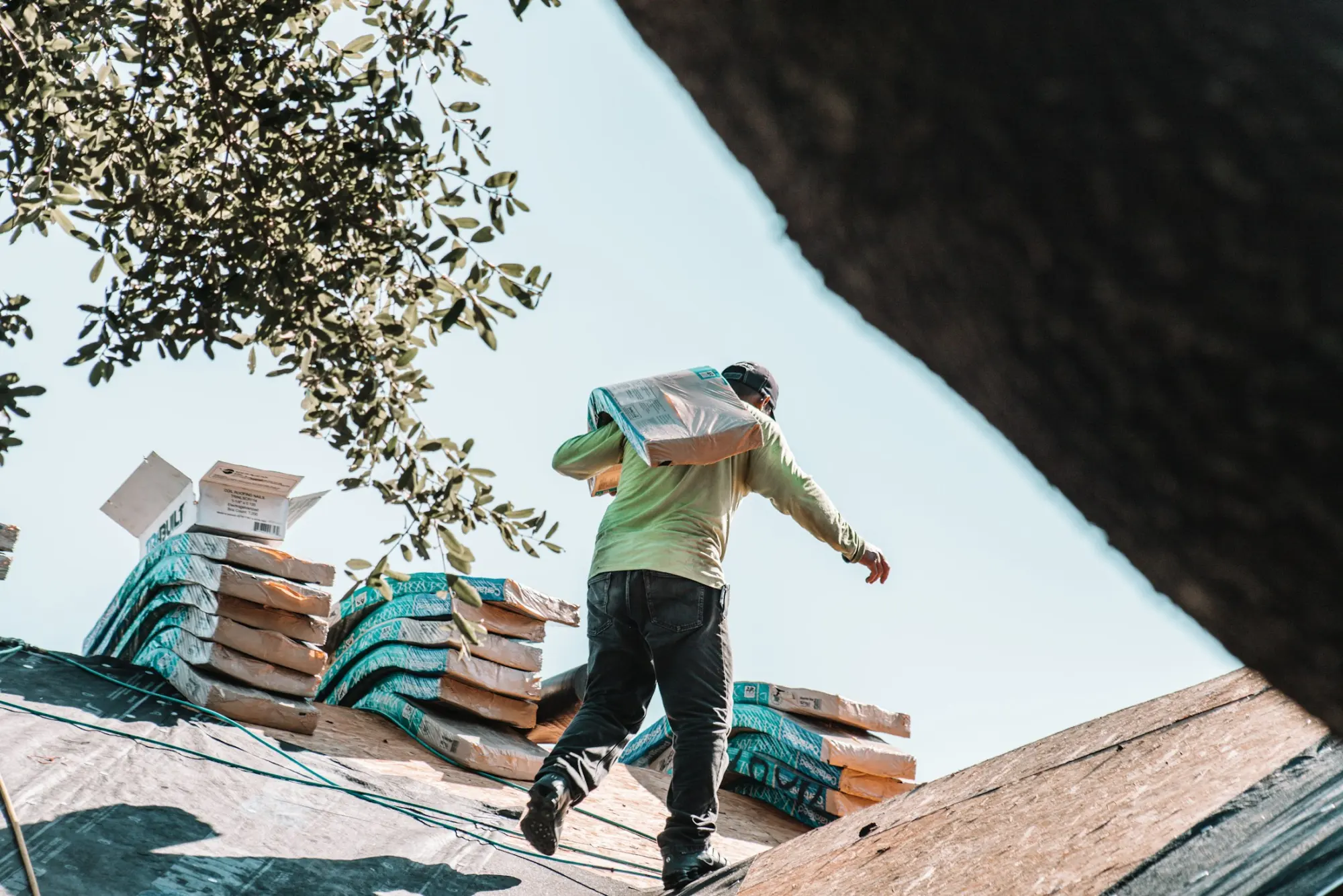 A roofer carrying bundles of shingles across a roof